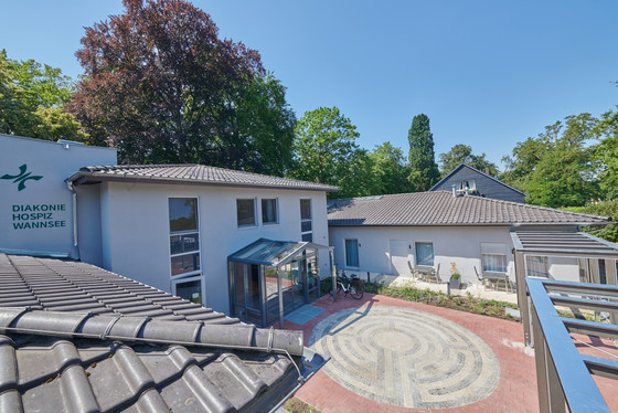Blick auf den Eingangsbereich mit Pflanzengerüst und Pflasterung vom Dachgeschoss des Stationären Diakonie Hospiz Wannsee in Berlin.