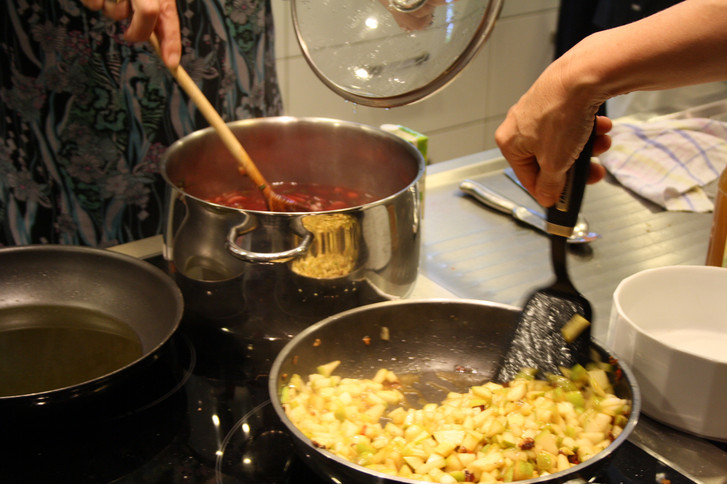 Eine Person rührt Sauce in Topf um und eine andere Person wendet mit Bratenwender Essen in Pfanne