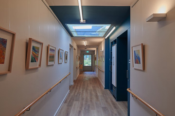 Ein heller Flur mit Holzboden, blauen Wandfarben, Tageslichtkuppeln und verschiedenen Gemälden an der Wand im Stationären Diakonie Hospiz Wannsee in Berlin-Wannsee. Ein heller Flur mit Holzboden, blauen Wandfarben, Tageslichtkuppeln und verschiedenen Gemälden an der Wand im Stationären Diakonie Hospiz Wannsee in Berlin-Wannsee.