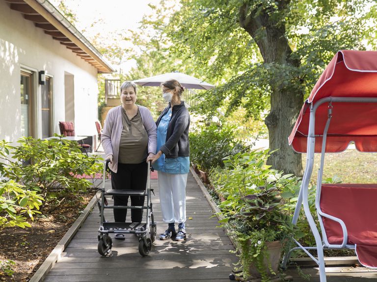 Diakonie Hospiz Wannsee - Eine Pflegerin begleitet eine Hospizgästin auf die von einem Park umgebene Terrasse des Diakonie Hospiz Wannsee. 