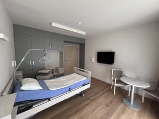 Blick in ein helles Gästezimmer mit einem frisch bezogenen Gästebett, Holzboden, hellen Wandfarben und Monitor an der Wand im Stationären Diakonie Hospiz Wannsee in Berlin-Wannsee. Blick in ein helles Gästezimmer mit einem frisch bezogenen Gästebett, Holzboden, hellen Wandfarben und Monitor an der Wand im Stationären Diakonie Hospiz Wannsee in Berlin-Wannsee.