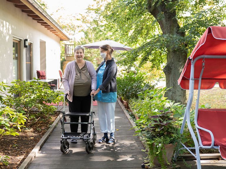 Diakonie Hospiz Wannsee - Eine Pflegerin begleitet eine Hospizgästin auf die von einem Park umgebene Terrasse des Diakonie Hospiz Wannsee. 